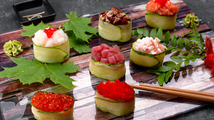Sushi maki in a cucumber, with caviar,tuna. scallop, eel, shrimp, eel and salmon, on a wooden board, with maple and acacia leaves, with shallow depth of field