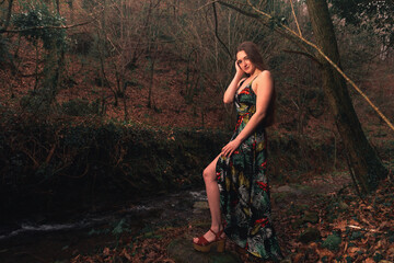 Young caucasian woman with a colorful dress in the middle of the forest next to a little river