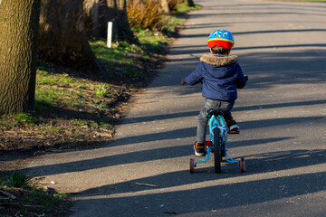 A small boy wearing a cycle helmet riding a bike in the park with stabilisers or stabilizers