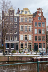 Obraz premium A winter scene of Amsterdam canal houses in the snow with ice on the water, vertical