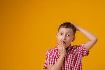 surprised boy, covering his mouth with his hand, stands on a yellow background. child does not want to talk, he learned a secret. The problem with the speech. Delayed speech development. Profanity.