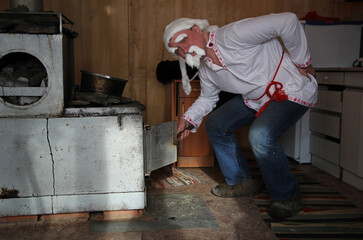 A man in an old man's suit near the Russian stove. Cosplay for the fairy tale Morozko.