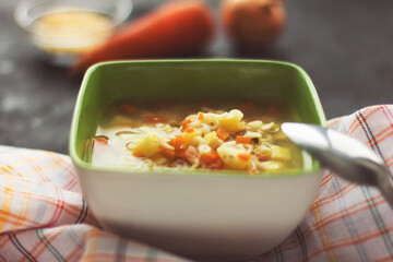 Chicken noodle soup with vegetables in a green plate, black background