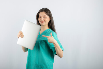 Fototapeta premium Photo of young nurse pointing at laptop on white background