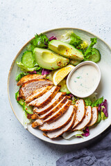 Grilled chicken salad with avocado, cucumber and dressing, top view. Healthy food concept.