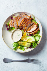 Grilled chicken salad with avocado, cucumber and dressing, top view. Healthy food concept.