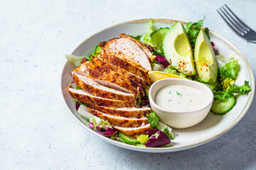 Grilled chicken salad with avocado, cucumber and dressing. Healthy food concept.