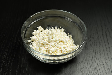 Grainy cottage cheese in a glass bowl on a black background close-up