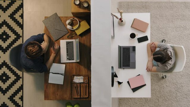 Top View Shot Of Young Man And Woman Sitting At Desks In Their Apartments Separated By Wall And Talking On Video Call On Their Laptops