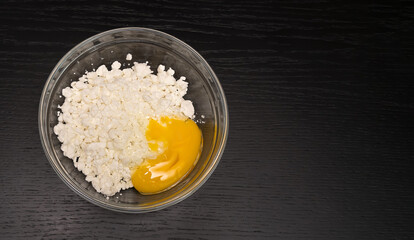 Grainy cottage cheese, egg in a glass bowl on a black table close-up with copy space, top view