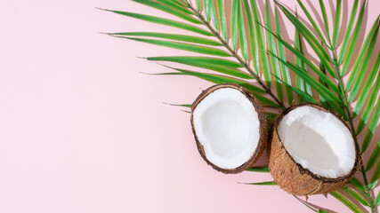 Obraz na płótnie Canvas Coconut halves with palm leaves on pink background. Organic cosmetics, food, summertime sale banner. Copy space for text or product place