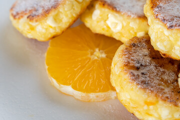 Close-up of cottage cheese pancake sprinkled with powdered sugar with orange circles. Beautiful background of a delicious, healthy breakfast