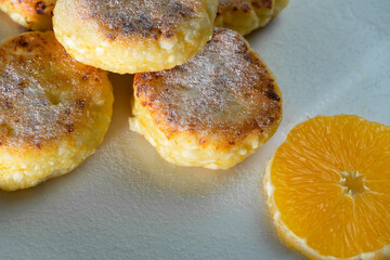 Delicious cottage cheese pancakes with powdered sugar, with an orange on a white plate close-up
