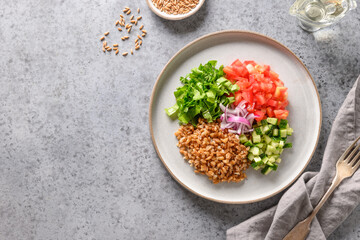 Not mixed salad of whole grain cereal spelt with ingredients and colorful vegetables on grey table. View from above.