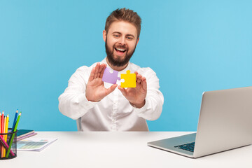 Happy smiling man office worker putting together two colored pieces of jigsaw, easily solving...