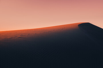 Fototapeta na wymiar Atmospheric and mystical moody light of the sunset sunbeam illuminated the slope of a sand dune somewhere in the depths of the Sahara Desert