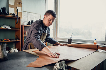 An experienced tanner at his master class shows how to work with leather, lays it out on the table.