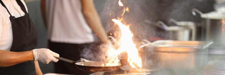 Cook in kitchen holds frying pan in which fire is burning. Cooking in restaurants and cafes concept