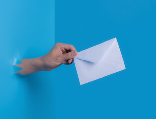 Man's hand holding envelope through the torn blue plastic background