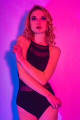 Fashion photo of young  girl on Colored background, studio shot. Beautiful blond woman with red lips curly hair. Woman in neon light. The girl in body dancing go-go, night club. Sexy swimsuit