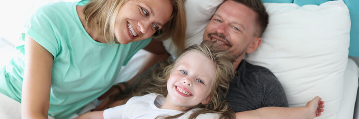 Family mom dad daughter lie in bed and smile. Raising children in harmony and love concept