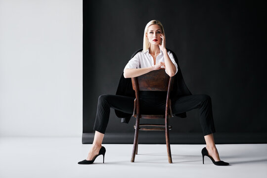 Fashion portrait of sensual trendy woman posing on retro chair against black studio background.