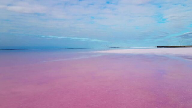 AERIAL, CLOSE UP: Flying close above smooth water surface of amazing pink lakes of Sivash, Ukraine. Beautiful red and violet saltworks on blue sky background. Stunning colorful salt evaporation ponds