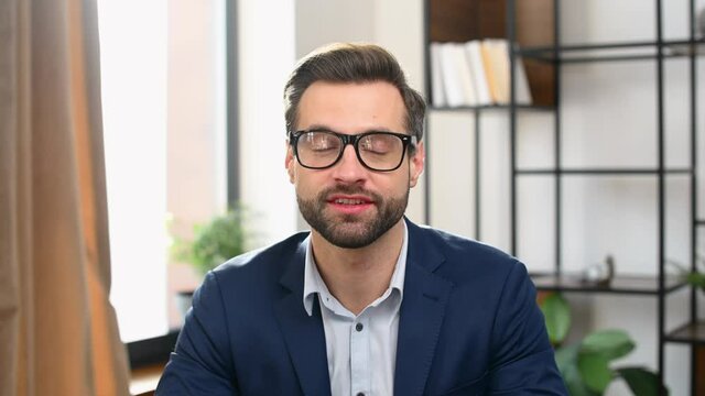 Young bearded businessman in formal clothes sitting at desk, talking at camera, introducing himself on online job interview, smart man presenting the idea during business video call. Webcam view