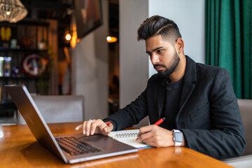 Young Indian businessman using a laptop during office break at cafe, relaxing with a cup of coffee.