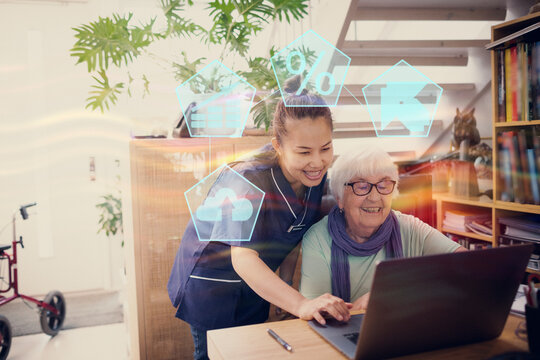 Home carer helping senior woman to use laptop
