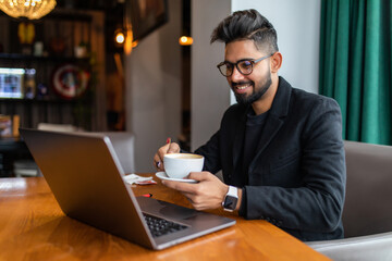 Young indian business man on laptop and coffee at a cafe