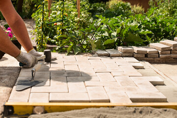 The master lays paving stones in layers. Garden brick pathway paving. Laying concrete paving slabs...