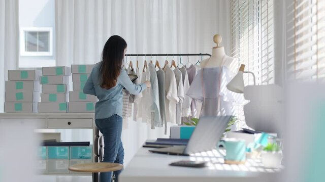 Young attractive beautiful hipster asia female fashion store owner use digital tablet check stock clothes or package box on rail rack at home office small SME business entrepreneur e-commerce concept.