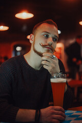 A man in a bar drinks beer, a handsome red-haired guy with a long mustache in a pub.