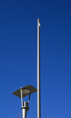 one flagpole without flag and one lantern on a background of azure blue summer sky