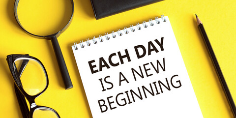 Notepad with the text EACH DAY IS NEW BEGINNING on a yellow background with glasses, a magnifying glass and a pencil. Business concept.