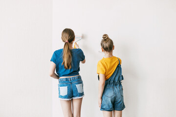 Obraz premium Two sisters are painting the walls of the house white, in denim overalls and a bright yellow T-shirt, home renovation