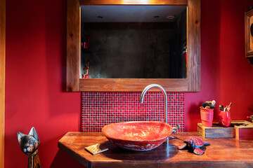 Interior of red bathroom with mirror on a wall, stylish ceramic wash basin on wooden counter and art decoration. Rustic bathroom in a cottage. 