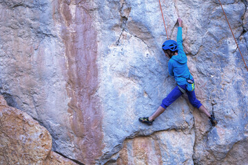 Fototapeta premium A woman in a helmet climbs a beautiful blue rock.