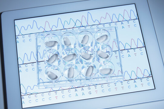 Pills in multiwell dish on digital tablet displaying DNA sequencing