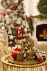 Christmas composition with decorative reindeer and candles on golden table in room