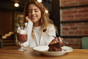 Positive woman eating cake and drinking coffee