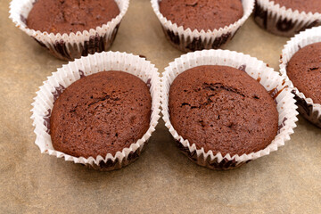 Brown chocolate muffins wrapped in white paper baked in the oven, lying on baking paper.