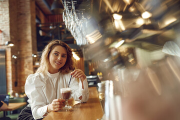 Dreamy woman drinking coffee while sitting on bar counter