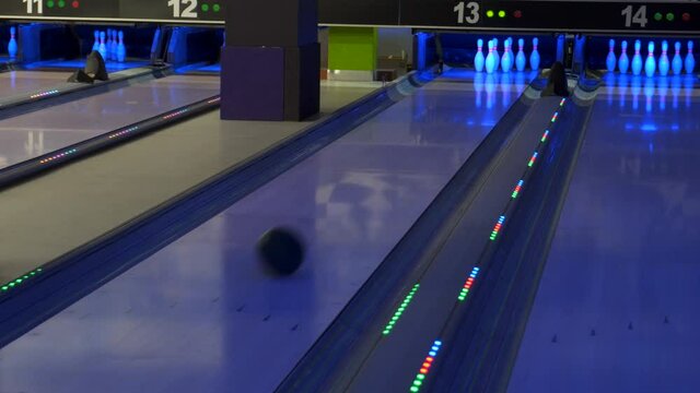 A bowling ball traveling down the lane and hitting pins at a Bowling alley.