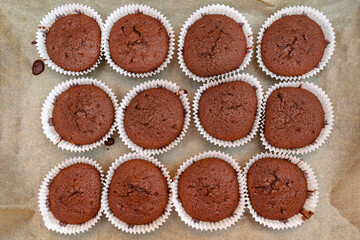 Brown chocolate muffins wrapped in white paper baked in the oven, lying on baking paper, top view.