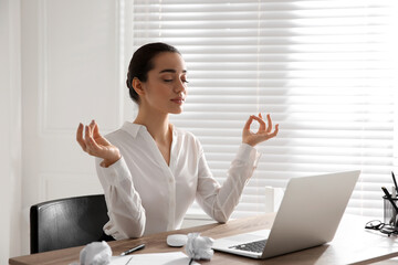 Young businesswoman meditating at workplace. Stress relief exercise - obrazy, fototapety, plakaty
