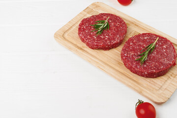 Two raw beef burger patties on wooden board