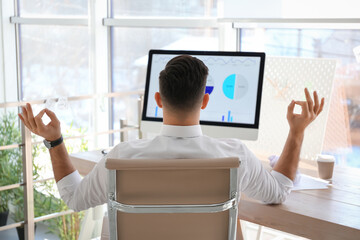 Businessman meditating at workplace in office, back view. Stress relieving exercise