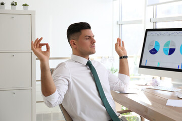 Businessman meditating at workplace in office. Stress relieving exercise